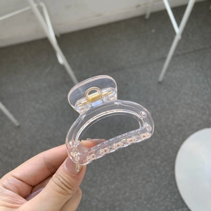 Hand holding a transparent pink butterfly hair claw clip with golden metal spring detail