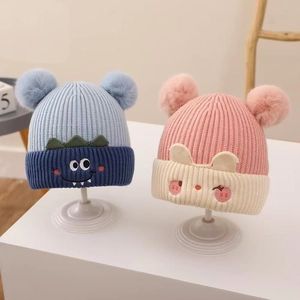 Detail view of baby knit hats featuring cute cartoon animal designs and soft fur pom-poms
