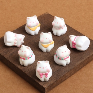 Set of eight miniature white resin cats with colorful floral collars on a wooden surface