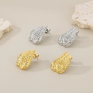 Detailed close-up of gold and silver hammered teardrop earrings on a minimalist stone