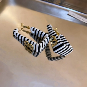 Detail of square faux leather earrings with golden B logo on a metallic tray