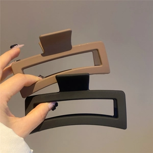 Hand holding large matte finish rectangular hair claws in beige and black colors