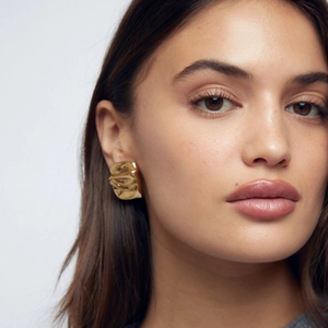 Close-up of a model wearing golden irregular wrinkled stud earrings with metallic luster