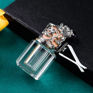 Close-up of a square glass car perfume bottle with silver crown lid and air vent clip