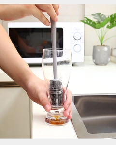 Detailed view of long handle silicone brush cleaning a tall glass bottle efficiently