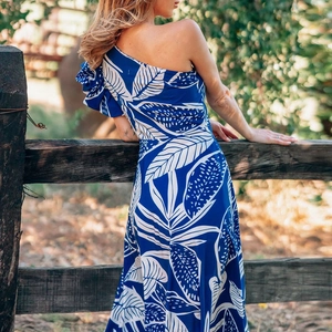 One-shoulder maxi dress with tropical blue and white leaf print in a sunlit resort setting