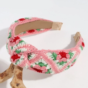 Close-up of pink hand-knitted floral headband with white and green crochet embroidery