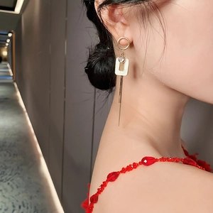 Asymmetric long tassel earrings with geometric cream squares and gold finish on model