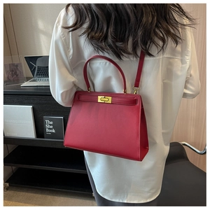 Detailed view of red leather handbag with gold metal clasp and adjustable shoulder strap