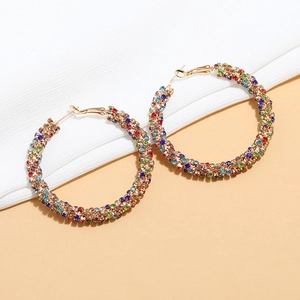Macro shot of large gold hoop earrings with multi-colored crystals on a neutral background