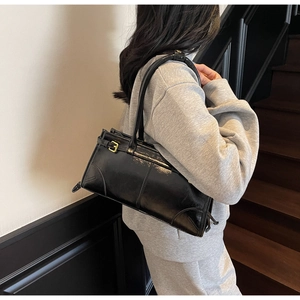 Glossy black patent leather tote bag with gold buckle detail worn by a model in a grey tracksuit