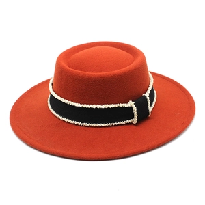 Detail of rust orange wool felt boater hat with black ribbon and white pearl trim