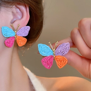 Macro detail of vibrant woven butterfly earrings featuring multi-color patterns and gold accents