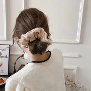 Close-up of floral beige corduroy scrunchie with lace trim on model's hair bun