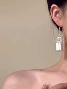 Détail de boucles d'oreilles à pompons argentés avec perle verte pour un look vintage