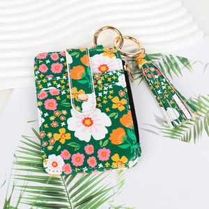 Detail view of a floral green card holder with gold ring and tassel charm on white background