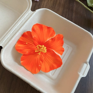 Detailed macro view of an orange hibiscus hair clip inside a white paper gift box