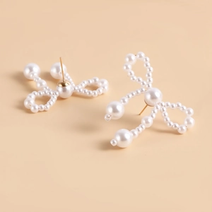 Macro shot of handmade bow earrings crafted from white imitation pearls on warm background