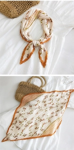 Dettaglio foulard plissettato con motivo floreale, bordi arancioni e trama leggera