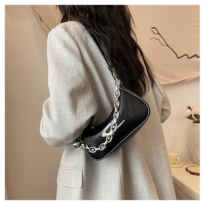 Detail of black pleated shoulder bag featuring a bold silver chain and metal logo charm