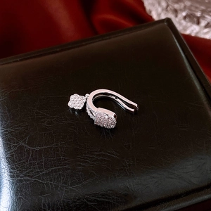 Macro shot of a silver swan ear cuff with sparkling zircon clover charm on black leather