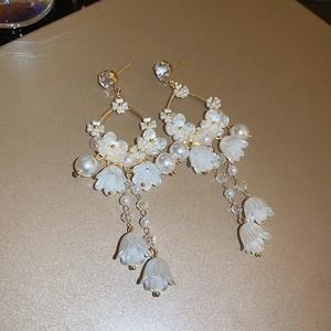 Elegant floral drop earrings with white resin petals and pearls on golden metal background