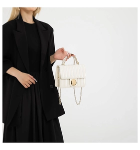 Detailed view of white quilted crossbody bag with gold chain and metal twist lock