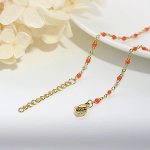 Close-up of golden titanium steel chain necklace with red beads and lobster clasp closure