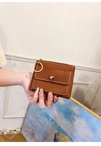 Detail of a brown leather coin purse with white stitching, gold ring, and snap pocket