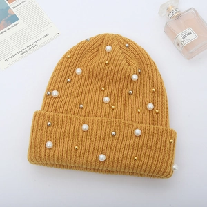 Close-up of ginger yellow knit beanie with white pearls and metal stud embellishments