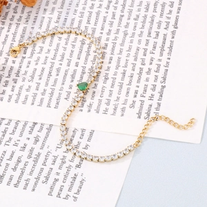 Detailed shot of golden tennis bracelet with white zircons and green pear-cut center stone