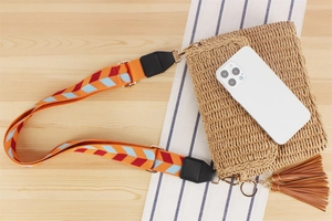 Handmade straw crossbody bag with colorful woven strap and brown tassel on wooden surface