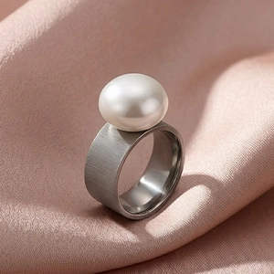 Detail of wide brushed stainless steel ring featuring a large elegant white pearl