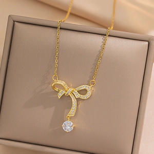 Elegant gold bow necklace with sparkling zircon pendant on soft fabric background