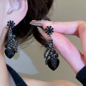 Close-up of elegant black heart-shaped earrings with diamond floral details on model