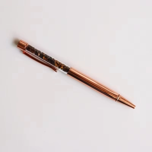 Detail of rose gold ballpoint pen with transparent top filled with brown tiger eye stones