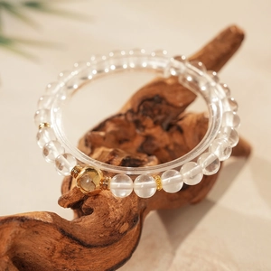 Detail of beaded white crystal bracelet with golden heart bead on natural wood base