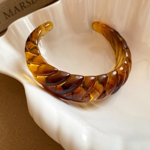 Macro detail of amber resin spiral bangle displayed on a white shell-shaped plate