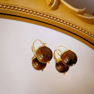 Close-up of vintage resin earrings with golden clips and textured brown beads on a mirror