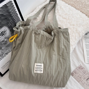Detail of sage green pleated tote bag fabric texture and logo label on white pillow