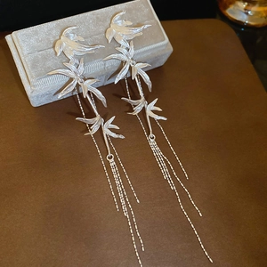 Detailed close-up of silver bamboo leaf earrings with long metal tassels on a brown surface