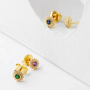 Close-up of geometric floral stud earrings with colorful zircon stones on white stone