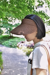 Detail of dark brown raffia sun visor with woven texture worn in a sunny garden setting
