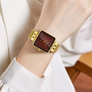 Close-up of a square gold watch with a deep red dial and mesh band on a wrist