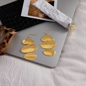 Détail de boucles d'oreilles pendantes dorées à trois couches sur un bureau au style moderne
