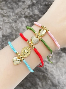 Close-up of handmade colorful braided bracelets featuring gold-plated heart pendants on wrist