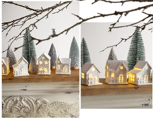 Close-up of lighted miniature white snow house and frosted Christmas trees decor