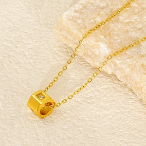 Minimalist gold cube pendant necklace with inset gemstone on light natural stone