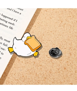 Detailed close-up of a cute white duck enamel pin with toast and a black rubber clutch