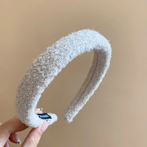 Close-up of beige bouclé fabric headband featuring a handmade label and soft texture